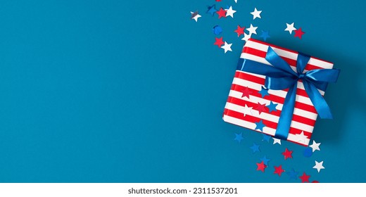 4th of July, USA Presidents Day, Independence Day, US election concept. Gift striped box with bow, star confetti on blue background. Flat lay, top view, copy space, banner - Shutterstock ID 2311537201