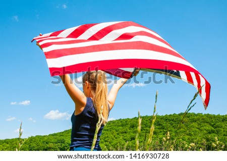4th of July. Young woman holding American flag on blue sky background. 