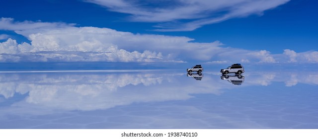 4WD car driving on the mirror surface of Uyuni Salt Flat with the reflection of sky and cloud, Bolivia