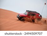 4x4 cars drift across Saudi Arabia’s striking red sand desert. The vehicles perform thrilling maneuvers, sending sand flying in dramatic arcs against the backdrop of the vast vibrant dunes near Riyadh