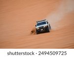 4x4 cars drift across Saudi Arabia’s striking red sand desert. The vehicles perform thrilling maneuvers, sending sand flying in dramatic arcs against the backdrop of the vast vibrant dunes near Riyadh