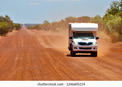 4x4 Offroad Camper Van Driving On Red Sand Gravel Road Highway Creating Dust In Australia Outback On A Sunny Day With Blue Sky And No Clouds