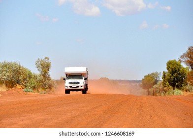 4x4 Offroad Camper Van Driving At High Velocity On Red Sand Gravel Road Highway Creating Dust In Australia Outback On A Sunny Day With Blue Sky And No Clouds