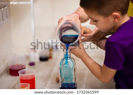 4-year-old boy adding colored water in a glass bottle for a science experiment. Density of liquids
