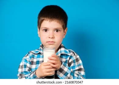 A 4-year-old boy holds a glass of milk on a blue background. The benefits and harms of milk for preschool children.