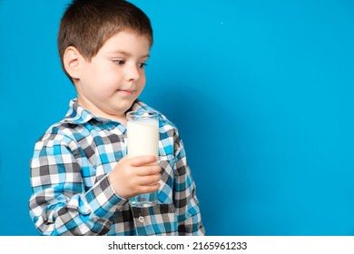 A 4-year-old boy holds a glass of milk and squirms looking into the camera. Cow's milk protein allergy, lactose intolerance, space for text.
