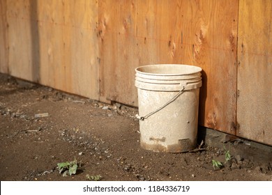 5 Gallon Bucket On Muddy Ground, Beside A Plywood Wall, With Space For Text On Top