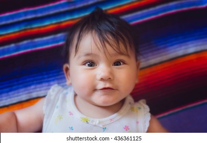 A 5 month old baby girl laying on a mexican blanket. 