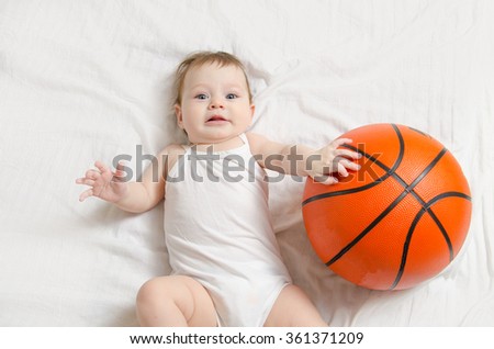 5 month old baby lying on his back on white sheet playing basketball