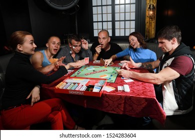 5 September 2019:Group Of People Playing Monopoly Board Game Together At Night.Friends With Funny Emotions Enjoying The Game In Evening 