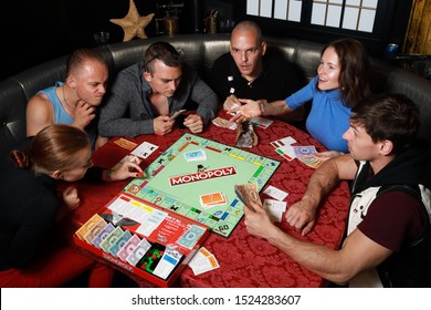 5 September 2019:Group Of People Playing Monopoly Board Game Together At Night.Friends With Funny Emotions Enjoying The Game In Evening.At Home Game. 