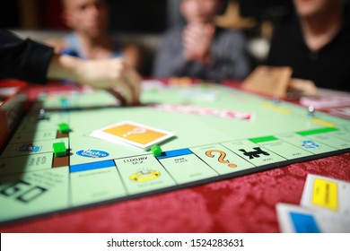 5 September 2019:Group Of People Playing Monopoly Board Game Together At Night.Friends With Funny Emotions Enjoying The Game In Evening.At Home Game. 