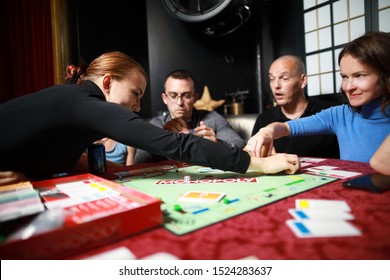 5 September 2019:Group Of People Playing Monopoly Board Game Together At Night.Friends With Funny Emotions Enjoying The Game In Evening 