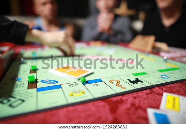5 September 2019:Group of people\
playing Monopoly board game together at night.Friends with funny\
emotions enjoying the game in evening.At home game.\

