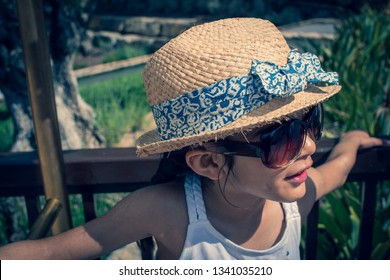 A 5 Year Old Girl In A Sunhat And Sunglasses Plays On The Luggage Rack Of A Bellboy, Outside A Holiday Hotel, Whilst On Vacation. 