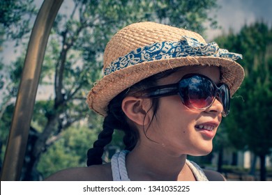 A 5 Year Old Girl In A Sunhat And Sunglasses Plays On The Luggage Rack Of A Bellboy, Outside A Holiday Hotel, Whilst On Vacation. 