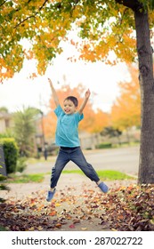5 Year Old Mixed Race Asian Caucasian Boy Does A Star Jump (jumping Jack) On The Footpath (sidewalk) Of His Suburban Neighborhood In Autumn (Fall)