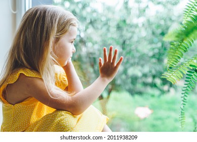 5 Years Old Blonde Girl Staring Out Of The Window On A Wet Cold Rainy Day.