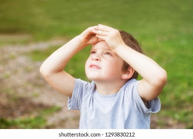 5 years old boy looks at the sky covering his eyes from the sun with his palms