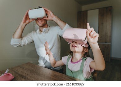 5 years old girl having fun time with her father using VR glasses at home for gaming or learning. Family activities concept. Modern technology using by family. Selective focus.
