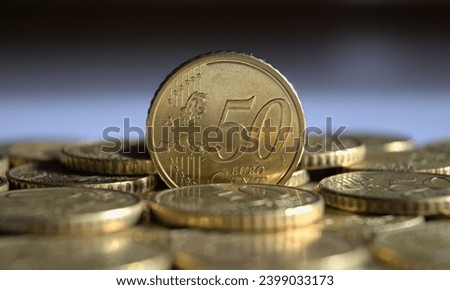 50 euro cent coin standing on the edge and facing the viewer with its face value (tails) and located on a small scattering of other 50 euro cent coins. Close up view.