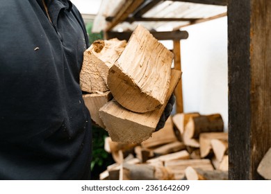 A 50 year old man has received a delivery of firewood and is putting the beech logs into the firewood rack. Outside the house, the rack is equipped with a roof to protect it from the weather. 