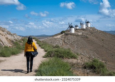 50 year old white woman walking down a dirt road towards the old white stone mills in Consuegra (Toledo, Spain) - Powered by Shutterstock