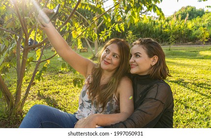 50 Year Old Woman Sharing With Her Beautiful Daughter In The Park. Mother And Daughter Take A Selfie