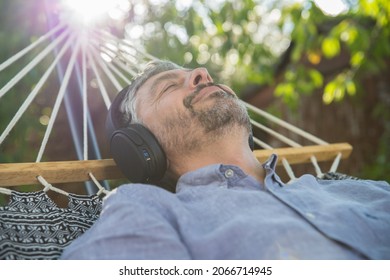 50 Years Old Man Relaxing In A Hammock And Listening Music With Headphones