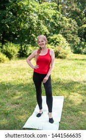 50 Years Old Woman Standing On A Mat Before Stretching Outdoors In A Park On A Grass.