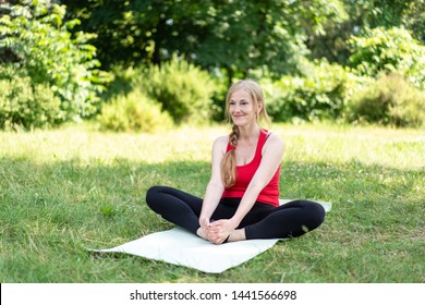 50 Years Old Woman Stretching Her Body On Grass In A Park On A Yoga Mat.