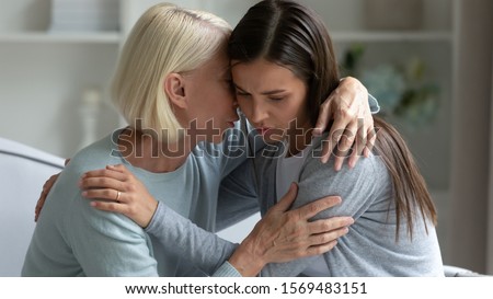50s elderly mother hugs calms grown up daughter telling on ear words supporting her, mom and adult child share secrets seated on couch. Trust, connection and help in difficult period of life concept