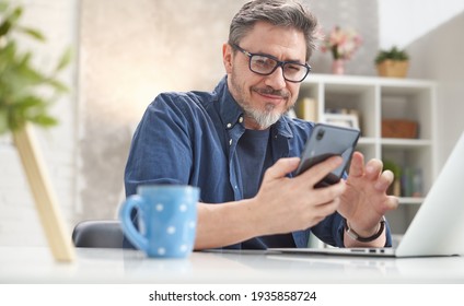 50s Man Checking News On Phone At Home. Confident Happy Smiling.