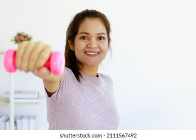 50s Old Mature Asian Woman Holding Dumbell With One Hand Showing Arm Strength With Happy And Self-confident Looking To Camera. Concept Of Life Balance, Good Health, And Wellbeing Of Elderly Female.