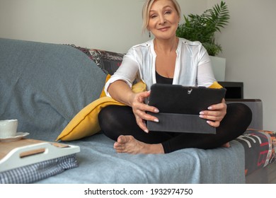 50s Years Old Woman Sit At Home On Sofa And Look To The Tablet, Drink Tea.