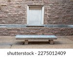 50th reunion dedication bench. Against a walk with pink stones and a window-shaped stone relief. Bench is isolated and empty.