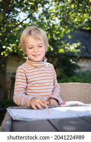 5-6 Year Old Child Learns To Read With Enthusiasm And Fun. Sits At A Table In The Garden. Reading Skills For Preschooler, Soon To School