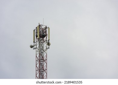 5G Communication Tower With Microwave Dish Antenna And Scaffolding With Ladder Inside Against A Cloudy Sky