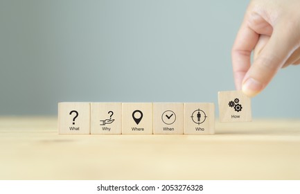 5W1H concept. Business framework and analysis. WHO WHAT WHERE WHEN WHY HOW Questions. The wooden cubes with 5W1H symbols and hand holds "how" cubes block. Beautiful grey background  and copy space. - Shutterstock ID 2053276328