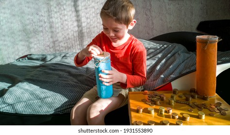 5-year-old Boy Puts Euro Cent Coin In Selfmade Piggy Bank,,sitting On Bed,wooden Nightstand With Scattered Coins Columns,sunny Day,hard Light, Shadows.Learning Financial Literacy.Selective Focus.