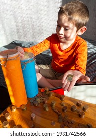 5-year-old Boy Puts Euro Cent Coin In Selfmade Piggy Bank,sitting On Bed,wooden Box With Scattered Coins Columns,sunny Day,hard Light,shadows.Learning Financial Literacy,money Savings.Selective Focus.