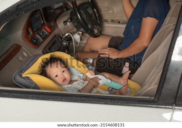 A 6 month old\
Asian baby girl sits on a car seat. On the seat of the car, where\
the mopher is the driver, for safety and compliance with the law.\
to baby and transportion\
concept.