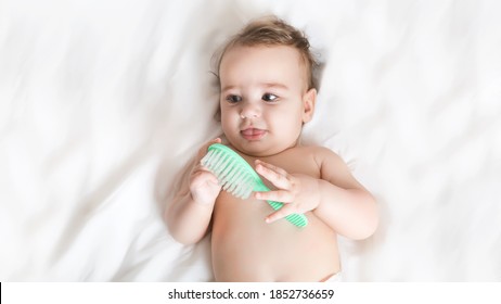 A 6 month old baby is holding a baby hairbrush and smiling. The child lies on a white bed. Funny toddler - Powered by Shutterstock