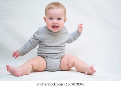  A 6 Month Old Baby Learns To Sit Down. Photo On A Neutral Background              