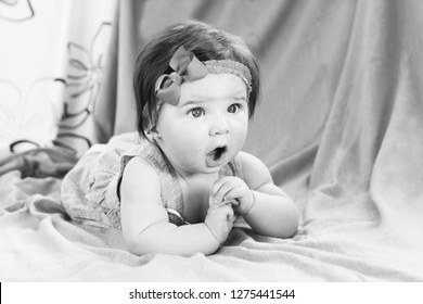 6 Months Old Child With Opened Mouth Lying On Her Front  With Amazed Face. Black And White Photo