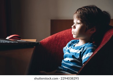 6 year boy attentively looking at laptop screen. Child watching horror video engrossed. Emotions of fear and horrible. Concept of useless content. Parental control. Bad effect on the psyche. Too near.