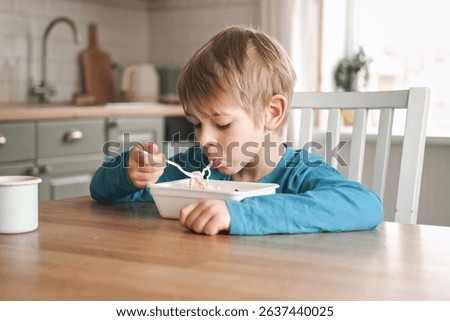 6 years old boy eats instant noodle from box. Child is eating spaghetti. Lunch time. A good appetite. Tasty children food. Close-up portrait. Carbs dinner. Fast food. Kid eating by himself with fork.
