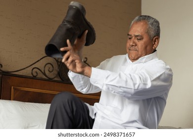 60 year old adult man sitting in a white shirt, getting ready on the bed in the hotel bedroom, putting on boots while relaxing in his room, preparing for business - Powered by Shutterstock