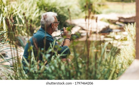 60 Year Old Man In Harmony With Nature, Taking Pictures On The Lake. Senile Depression And Loneliness.