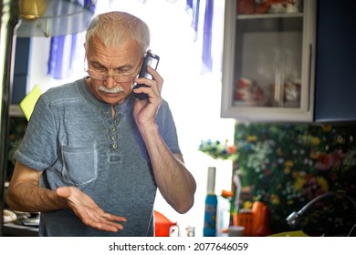 60 Year Old Man In Home. Serious Old Man With Smartphone Indoor. Indoors Portrait Of Senior Business Man Using Mobile Phone. Thin Gray-haired Elderly Man With Cell Phone Gestures Excitedly